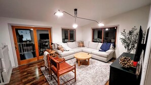 Een moderne woonkamer met een hoekbank, een houten salontafel, een houten stoel en een zwarte tv-meubel.