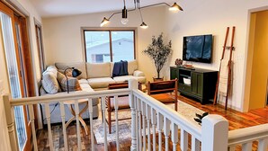 Een woonkamer met een bank, een televisie, een plant en een houten vloer.