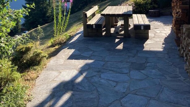 A stone patio with wooden benches and a table, surrounded by greenery and mountains in the background. - Outside: 4-room chalet for 6 (or even 7) people, with balconies, unobstructed view, very well locate (St-Luc)