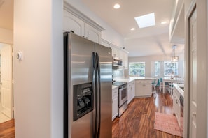 A modern kitchen with stainless steel appliances, white cabinetry, and a wooden floor.