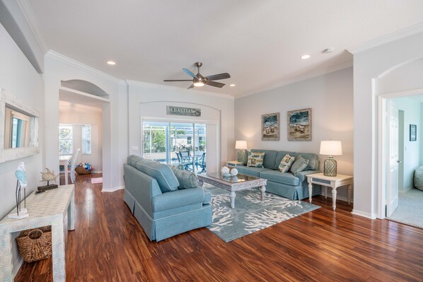 A spacious living room with a blue sofa set, a coffee table, and a ceiling fan.