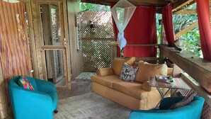Une pièce chaleureuse avec un plancher en bois, un canapé beige agrémenté d’un coussin, un fauteuil turquoise et une petite table sur laquelle se trouve une tasse.