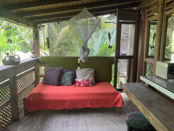 Ein Bett mit roter Bettdecke, mehreren Kissen und einem hängenden Moskitonetz.