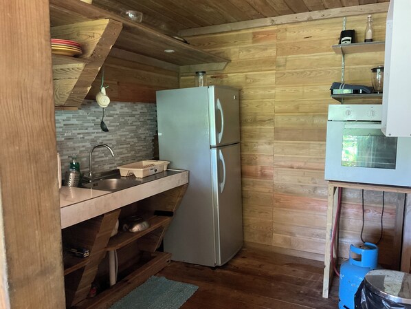A compact kitchen with a refrigerator, sink, and wooden shelves. - Bauhinia Tropical 2 bedroom Retreat Cottage (Trafalgar Road)