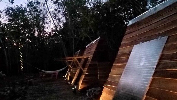 Une rangée de cabanes en bois aux toits inclinés, chacune éclairée par de petites lumières, nichée dans un espace boisé.