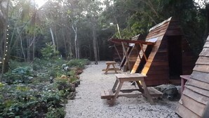 Une cabane en bois rustique, dotée d’un toit en pente, entourée d’un chemin de gravier et d’une végétation luxuriante.