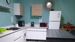 Una cocina compacta con armarios blancos, lavadora, microondas y refrigerador.