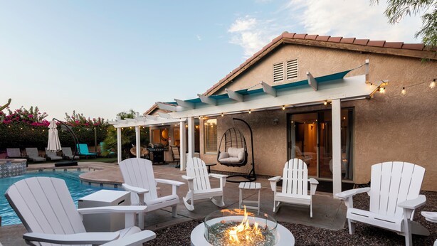 Een terras buiten met witte Adirondack-stoelen, een vuurkorf en een zwembad.