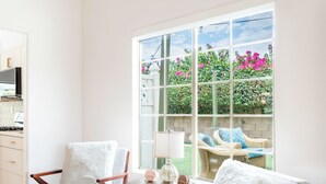 Een kamer met twee witte fauteuils, een klein tafeltje en een raam met uitzicht op een tuin.