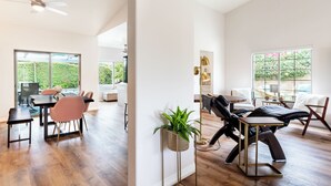Een ruime woonkamer met een eettafel, stoelen, een massagestoel en een plant.