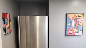 Een hoek kamer met een roestvrijstalen koelkast, houten vloeren en twee abstracte schilderijen aan de wanden.