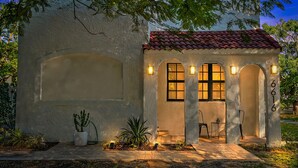 Un edificio con techo de tejas, ventanas arqueadas y un pequeño porche con sillas y una mesa.