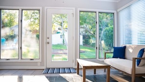 Valoisa olohuone, jossa on puinen penkki, valkoinen sohva sinisillä koristetyynyillä ja suuret, liukuvat lasiovet, jotka johtavat takapihalle.