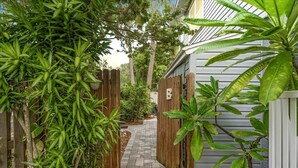 A narrow pathway flanked by wooden fences and lush greenery, leading to a building with a white exterior.