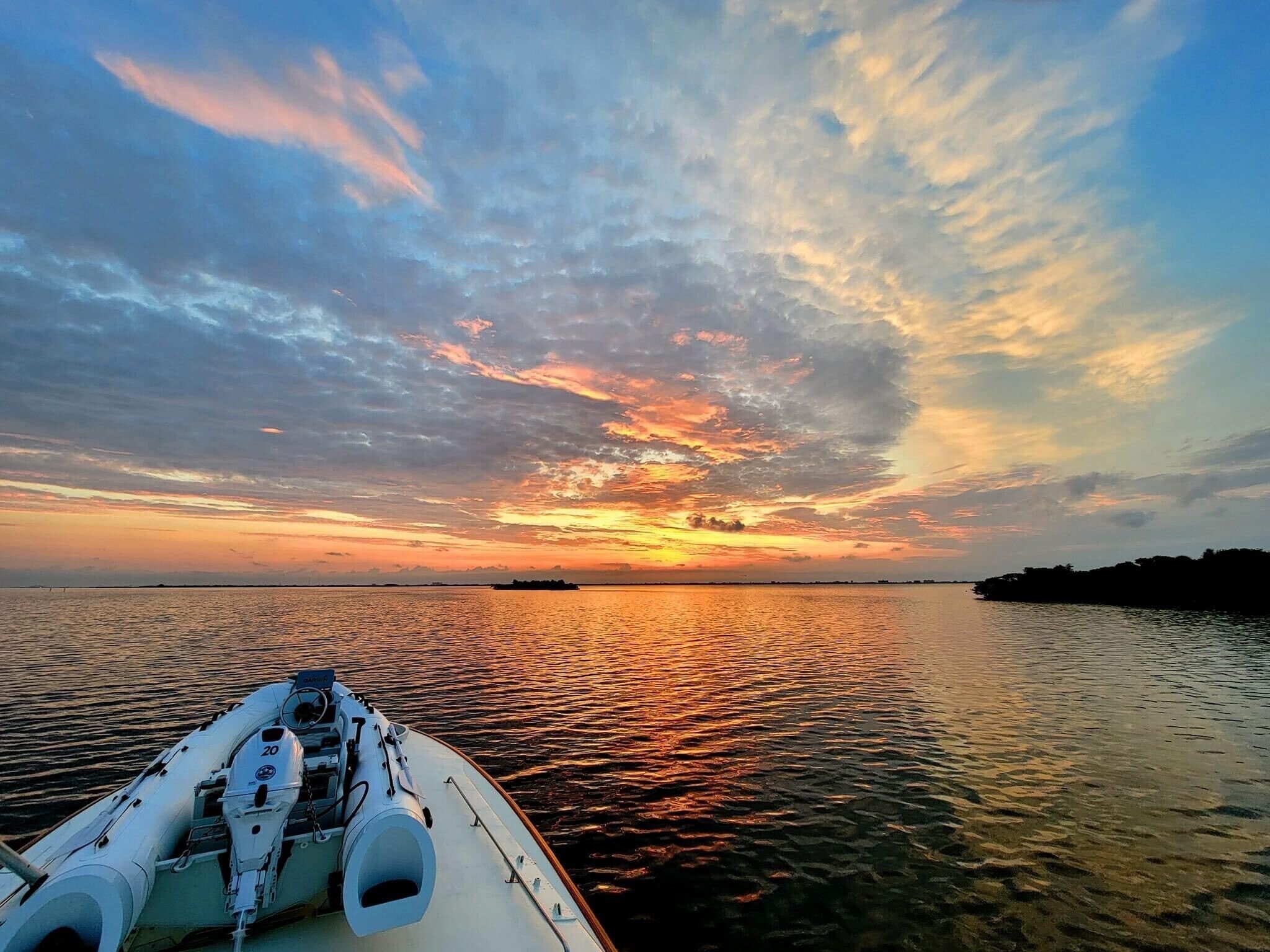A boat's bow with a water view, calm sea, and a sunset with clouds.