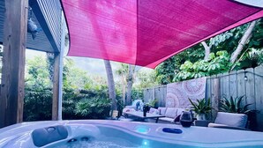 A hot tub area with a wooden deck, lounge chairs, and a large pink canopy.