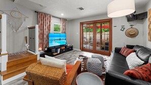 A modern living room with a flat-screen TV, a sofa, a coffee table, and a staircase leading to another level.