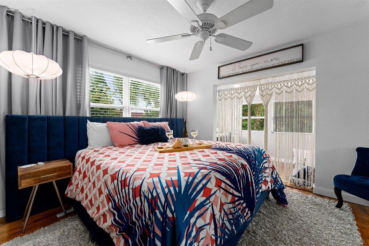 A bedroom with a bed, a nightstand, a chair, a ceiling fan, and a window with curtains.