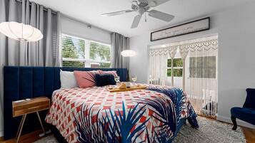 A bedroom with a bed, a nightstand, a chair, a ceiling fan, and a window with curtains.