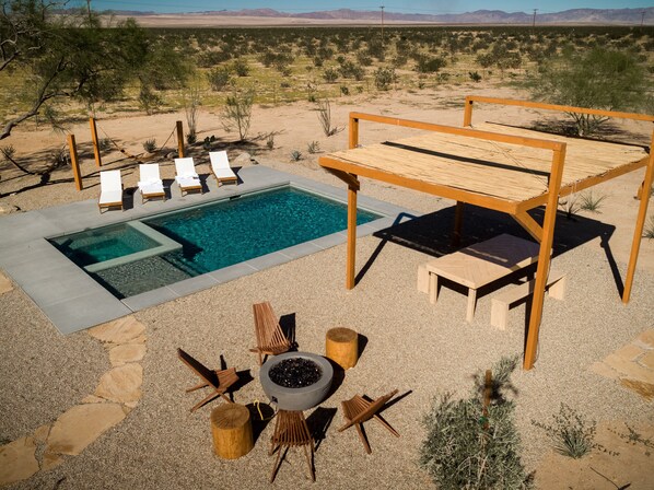 Un área de piscina con sillones de descanso, una chimenea y una pérgola de madera.