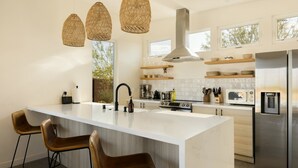 A modern kitchen with a large island, stainless steel appliances, wicker pendant lights, and wooden bar stools. - Casa Bella - Private Getaway w/ Pool - Spa - Views (Landers)