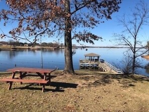 A lakeside picnic area with a wooden bench and a gazebo.