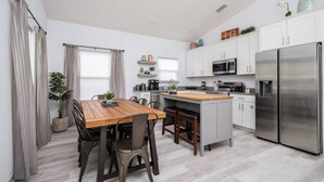 Une cuisine moderne avec des meubles blancs, des appareils en acier inoxydable, une table à manger en bois et un grand îlot central.