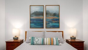 Une chambre à coucher avec un lit, deux tables de chevet, deux lampes et deux tableaux encadrés accrochés au mur.