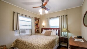 Ein Hotelzimmer mit einem Bett, einem Nachttisch mit Lampe, einem Holztisch und einem Deckenventilator.