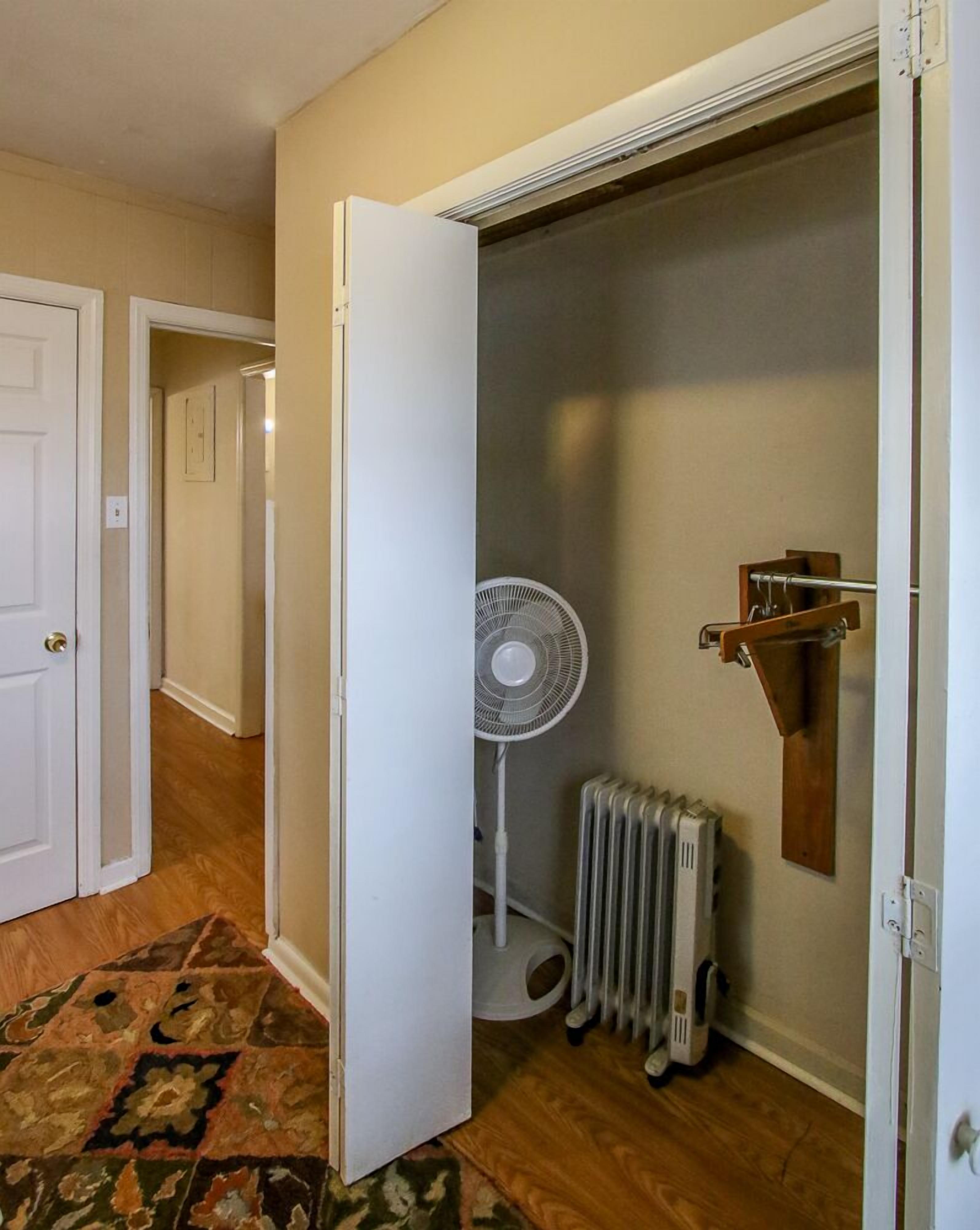 Un couloir avec une porte blanche, un radiateur et un ventilateur sur pied.