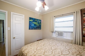 Quarto com cama, porta, ventoinha no teto, janela com persianas e pintura na parede.