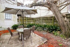 A patio with a round table and chairs, an umbrella, and a wooden fence. - The Savannah Belle Forsyth Park A Side (Savannah)