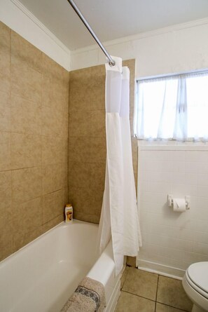 A bathroom with a bathtub, a toilet, and a window with curtains. - The Savannah Belle Forsyth Park A Side (Savannah)