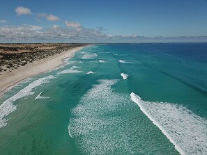 An aerial view of a beach with clear turquoise waters and white waves, sandy shore, and rocky terrain. - A new coastal home to relax & escape to, on the beautiful Yorke Peninsula in SA. (Marion Bay)