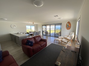 A spacious living area with a red sofa, a dining table, and a kitchen area. - A new coastal home to relax & escape to, on the beautiful Yorke Peninsula in SA. (Marion Bay)