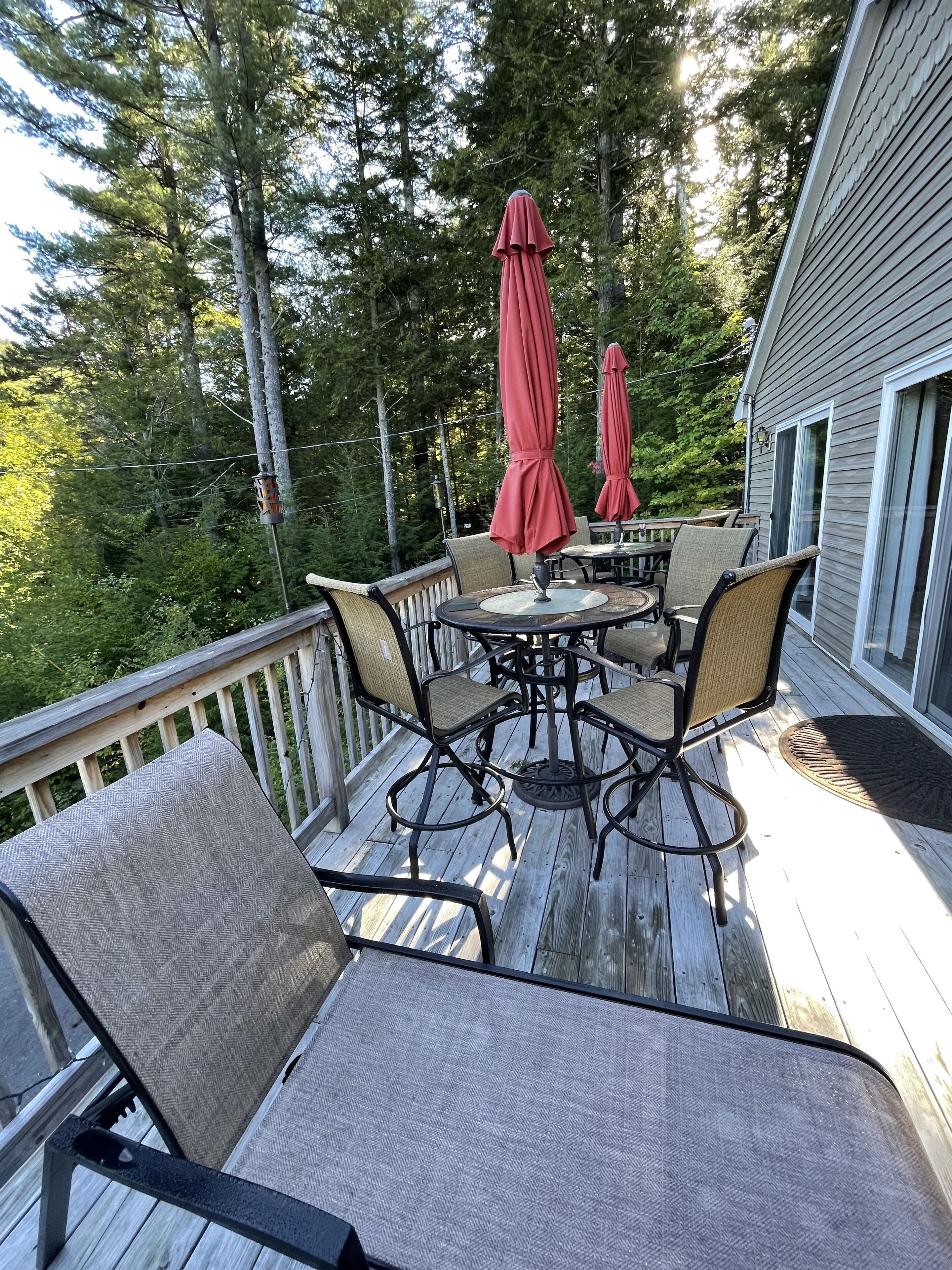 Eine Holzterrasse mit Gartenmöbeln, darunter Stühle und ein Tisch, umgeben von Bäumen.