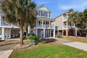 A two-story beachfront property with a covered porch, a balcony, and a small garden area.
