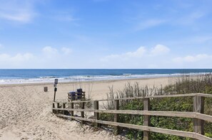En træpromenade der fører til en strand med kig til havet og et skilt.