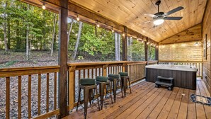 A wooden deck with a hot tub, bar stools, and a ceiling fan.