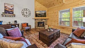 A cozy living room with a fireplace, wooden walls, and a large window.