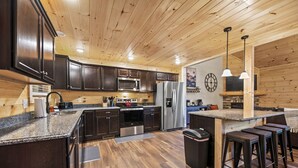 A modern kitchen with dark wood cabinets, stainless steel appliances, and a wooden ceiling.