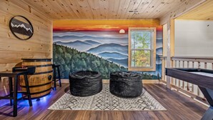 A wooden interior with a mural of mountains and a sunset, two black bean bags, and a wooden barrel table.