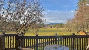 A wooden deck with a round table and two chairs, overlooking a grassy field and trees. - Unique renovated 4 bedroom home on private corner lot (Forks)