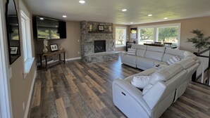 A spacious living room with a stone fireplace, a large white sofa, and a flat-screen TV mounted on the wall. - Unique renovated 4 bedroom home on private corner lot (Forks)