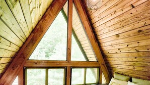 A cozy attic bedroom with a sloped ceiling, large windows, a bed with multiple pillows, and a hanging light fixture. - Dog Friendly Smoky Mts A-Frame with Views and Modern Decor (Sylva)