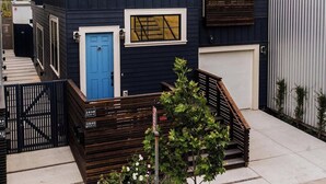 A modern two-story house with a dark exterior, a blue door, and a small front yard with a wooden bench and a tree. - 4 BR Luxury Designer Home Hot Tub, Parking Garage Near San Francisco UC Berkeley (Oakland)