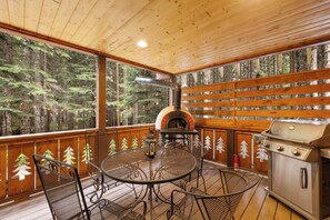 Eine Holzterrasse mit Pizzaofen, Grill und Metalltisch mit Stühlen.