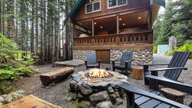 Una cabaña con un hogar de piedra, terraza de madera y asientos exteriores.