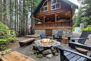 A lodge with a stone fire pit, wooden deck, and outdoor seating. - Snoqualmie Pass Ski Cabin w/Hot Tub and Bonus Tree House! (Snoqualmie Pass)
