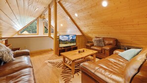 Interior acogedor de una cabaña de madera, con techo de madera, un televisor, sofás de cuero y una mesa de centro de madera.